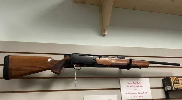 Long rifle mounted on a wall display, with wooden stock and black barrel.