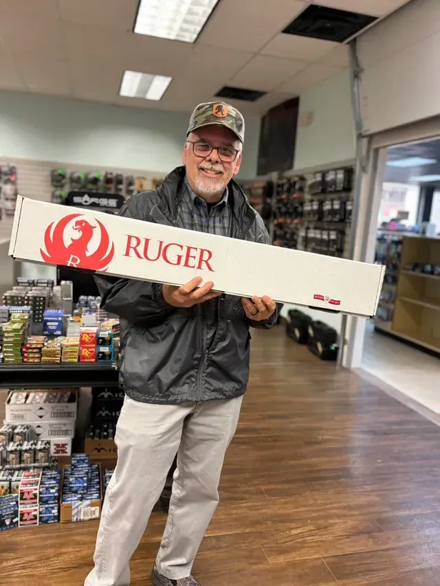 Man holding a Ruger rifle box inside a gun store. He's smiling.