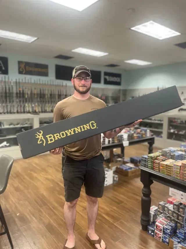 Man holding a long, black Browning gun case inside a gun store.