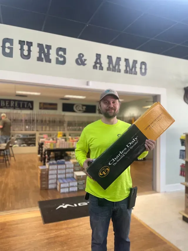 Man holding a large black-and-gold box inside a Guns & Ammo store