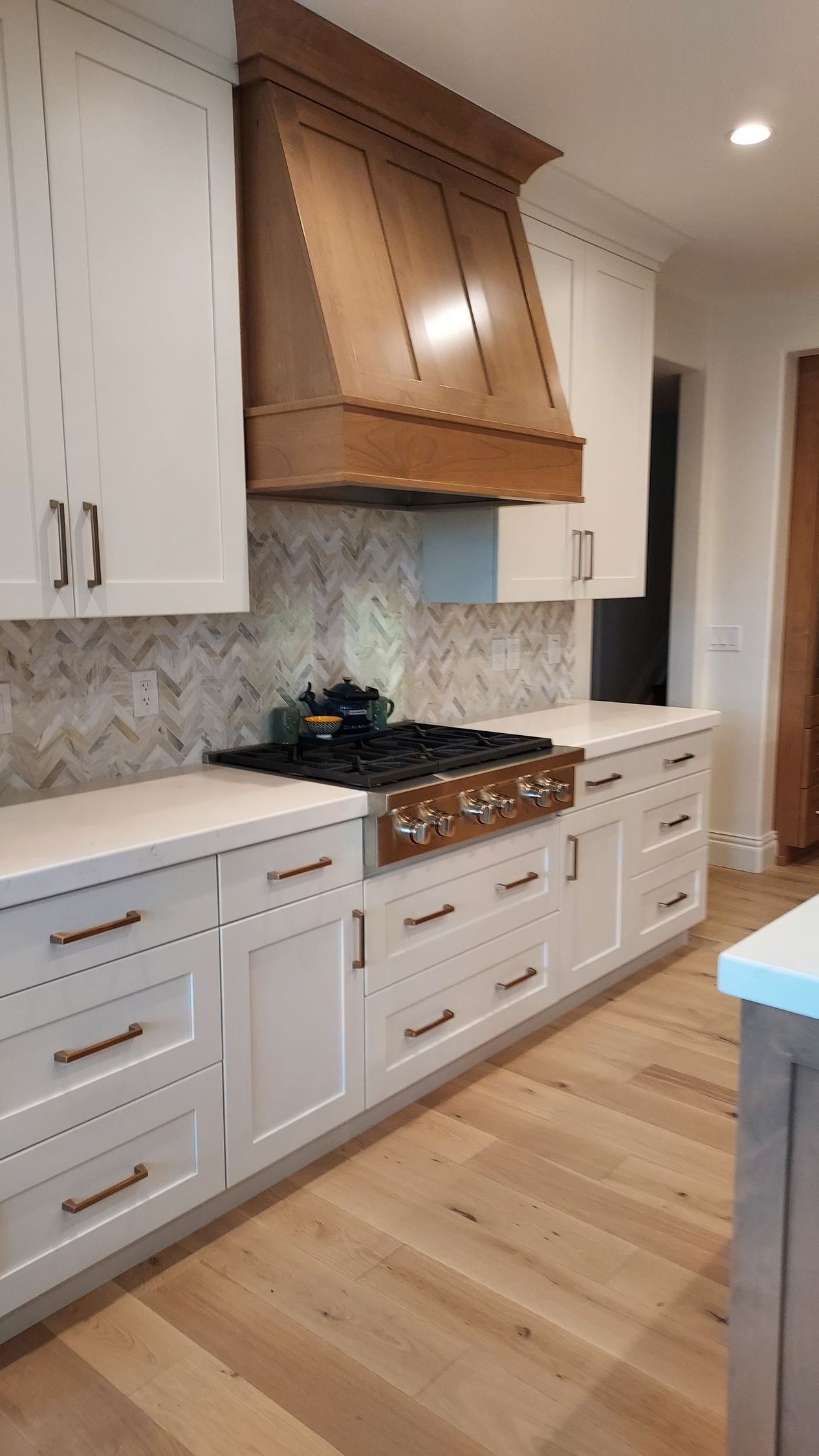 Kitchen with white cabinets, wood range hood, and beige countertops and backsplash.