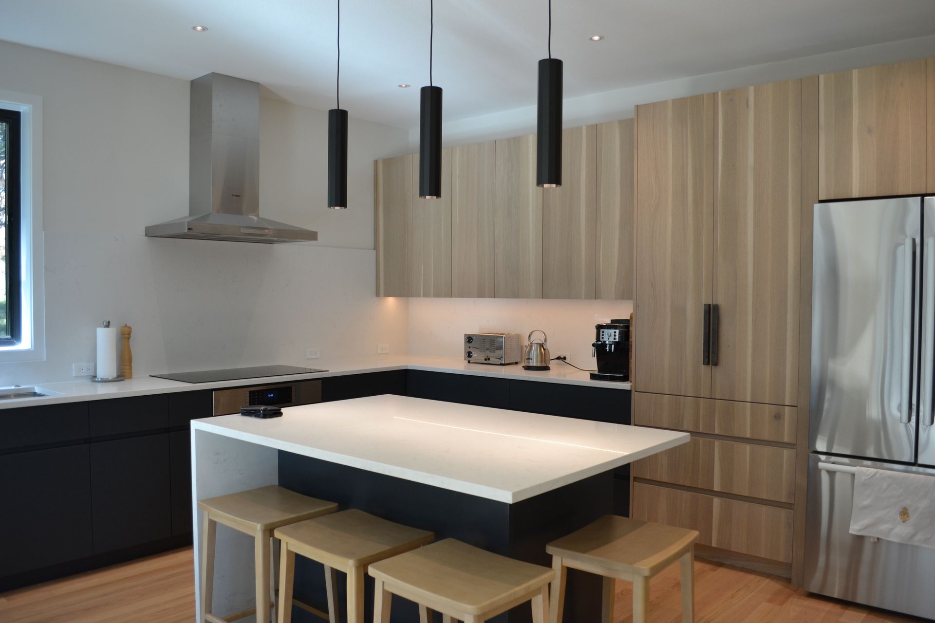 Modern kitchen with light wood cabinets, black island, stainless steel appliances, and hanging black lights.