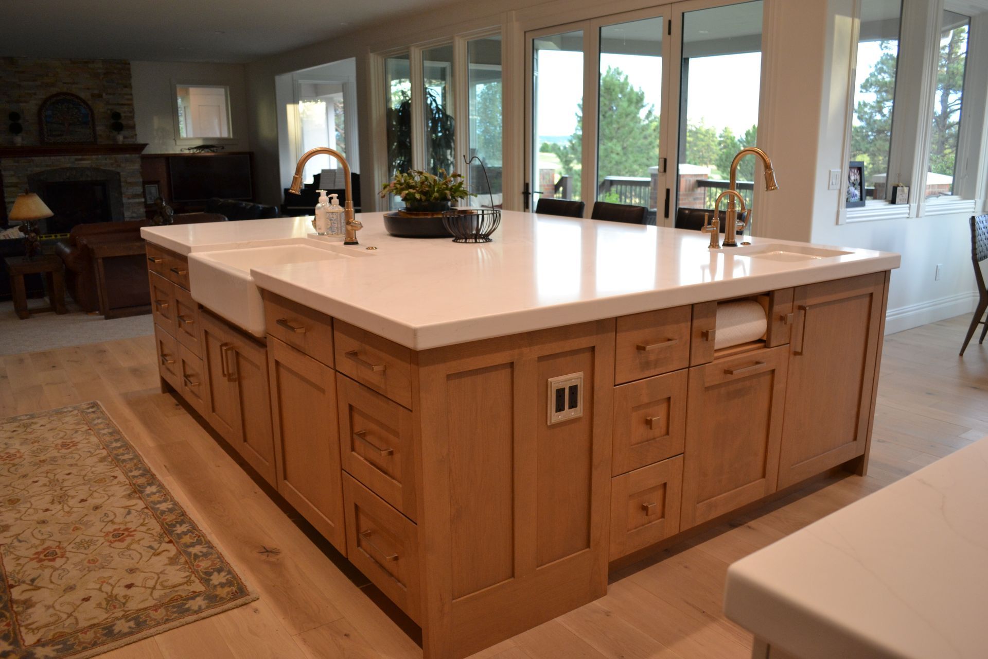 Large kitchen island with light wood cabinets and white countertop, featuring sinks and gold faucets.