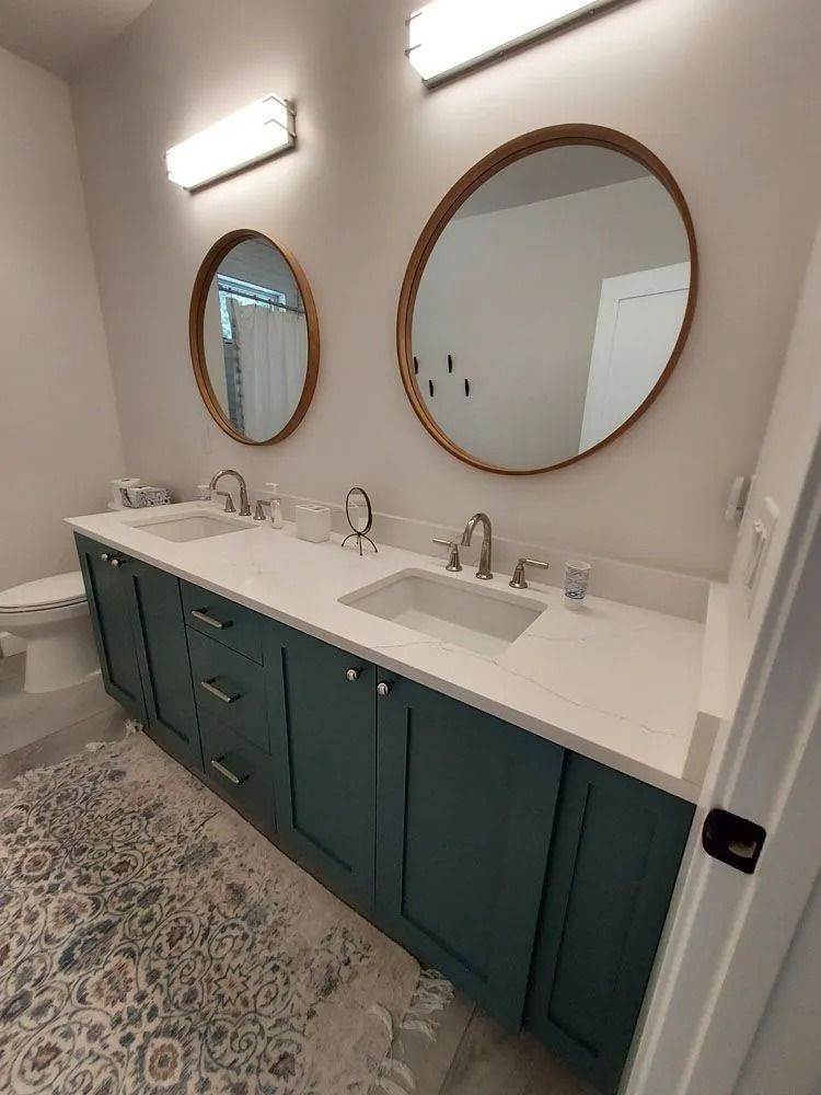 Bathroom with teal vanity, white countertop, round mirrors, and silver fixtures.