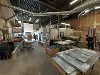Warehouse workspace with stacked materials, tools, and two people in the background