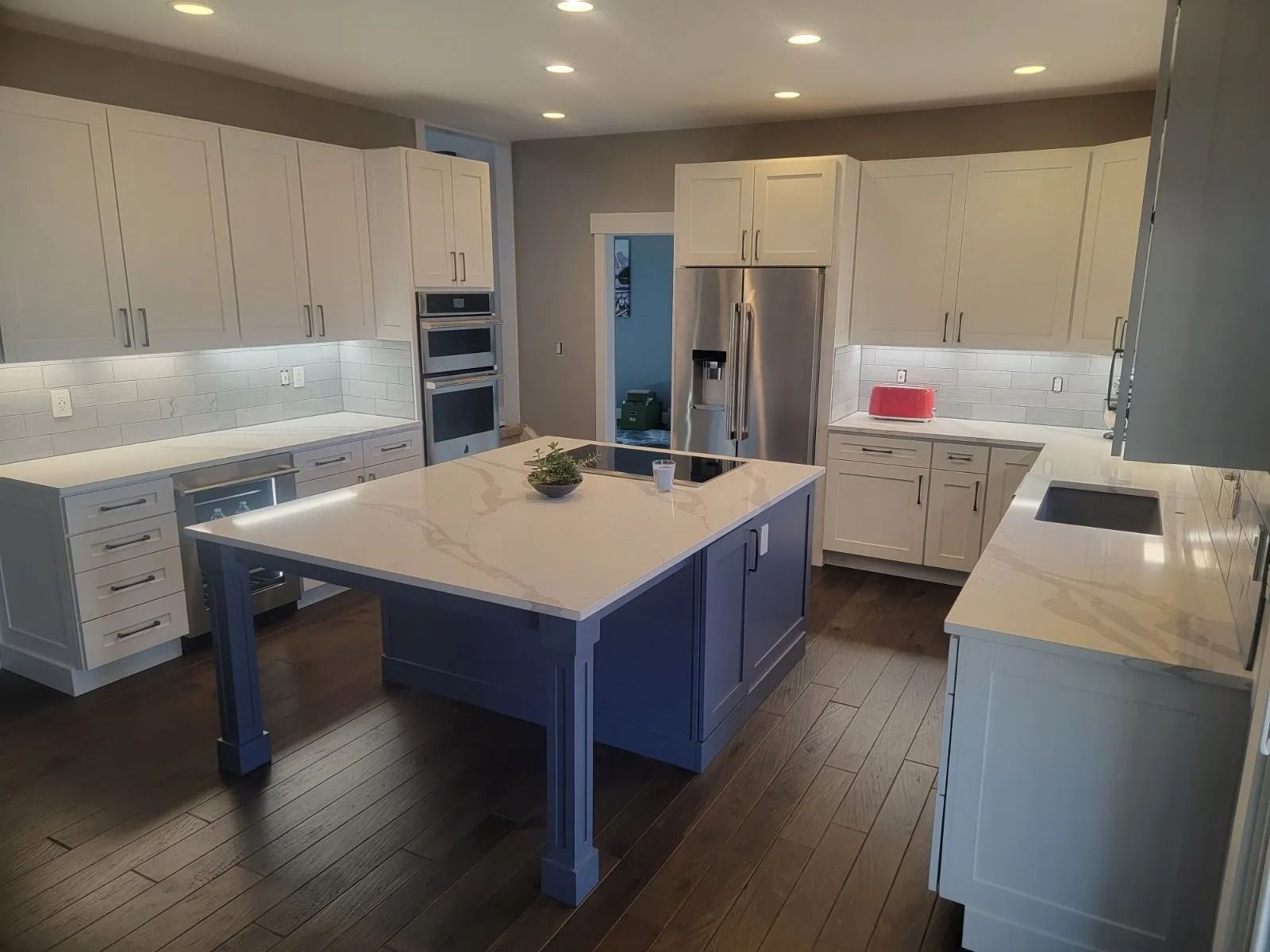 Modern kitchen with white cabinets, blue island, and dark wood floors.