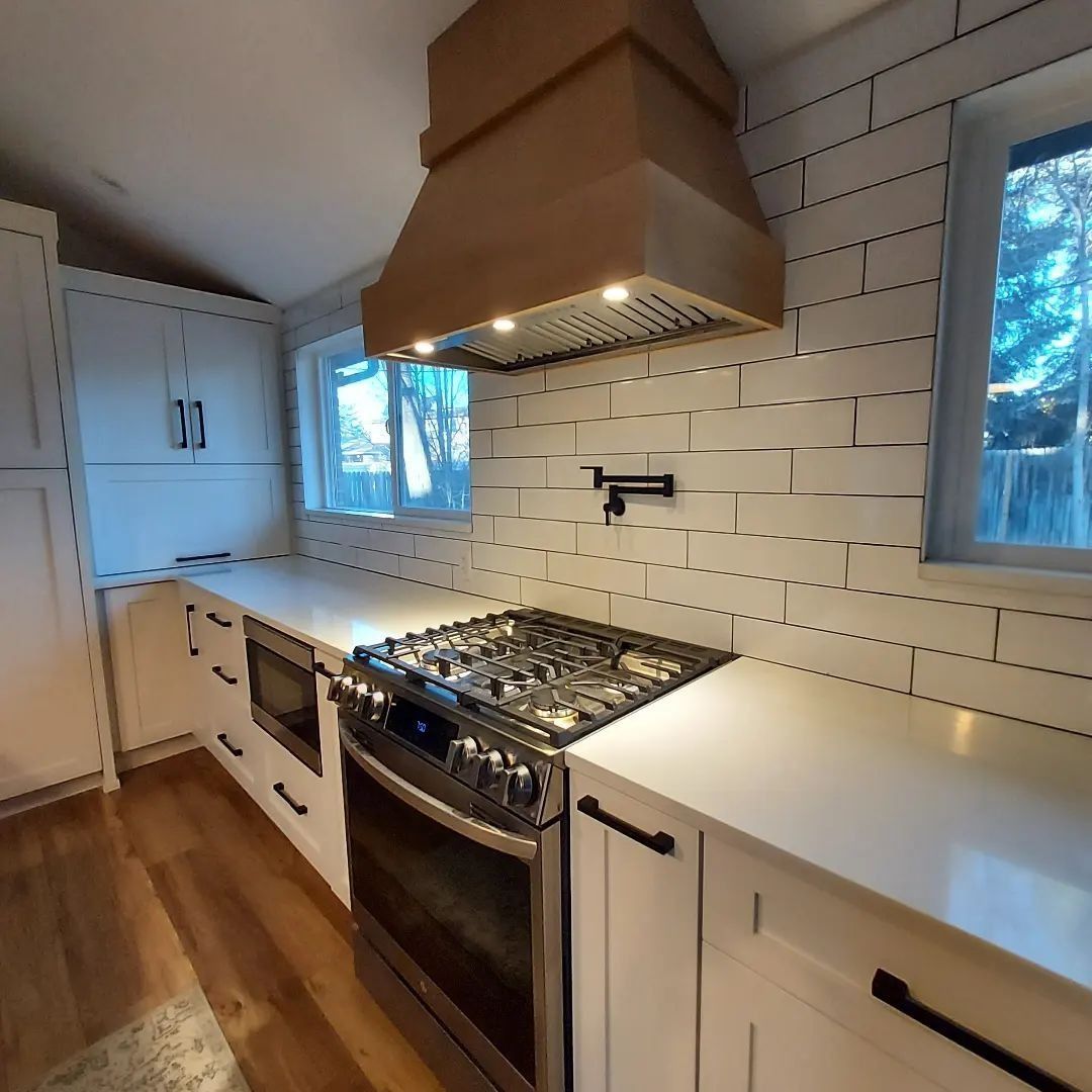 Modern kitchen with white cabinets, light wood range hood, gas stove, and white subway tile backsplash.