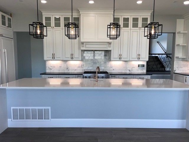 Modern kitchen with white cabinets, light blue island, and geometric pendant lights.