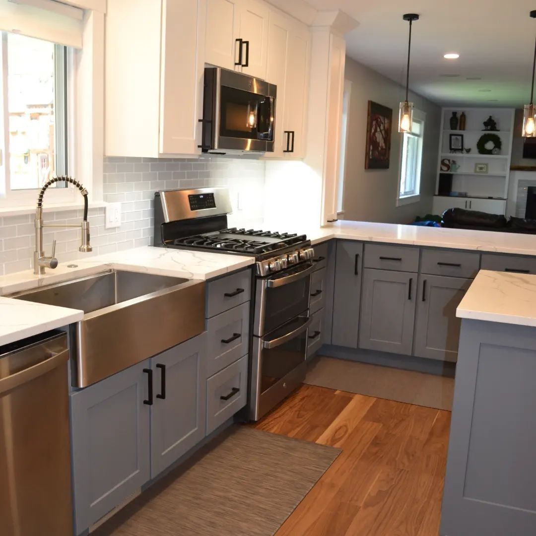 Modern kitchen with white and gray cabinets, stainless steel appliances, and wood flooring.