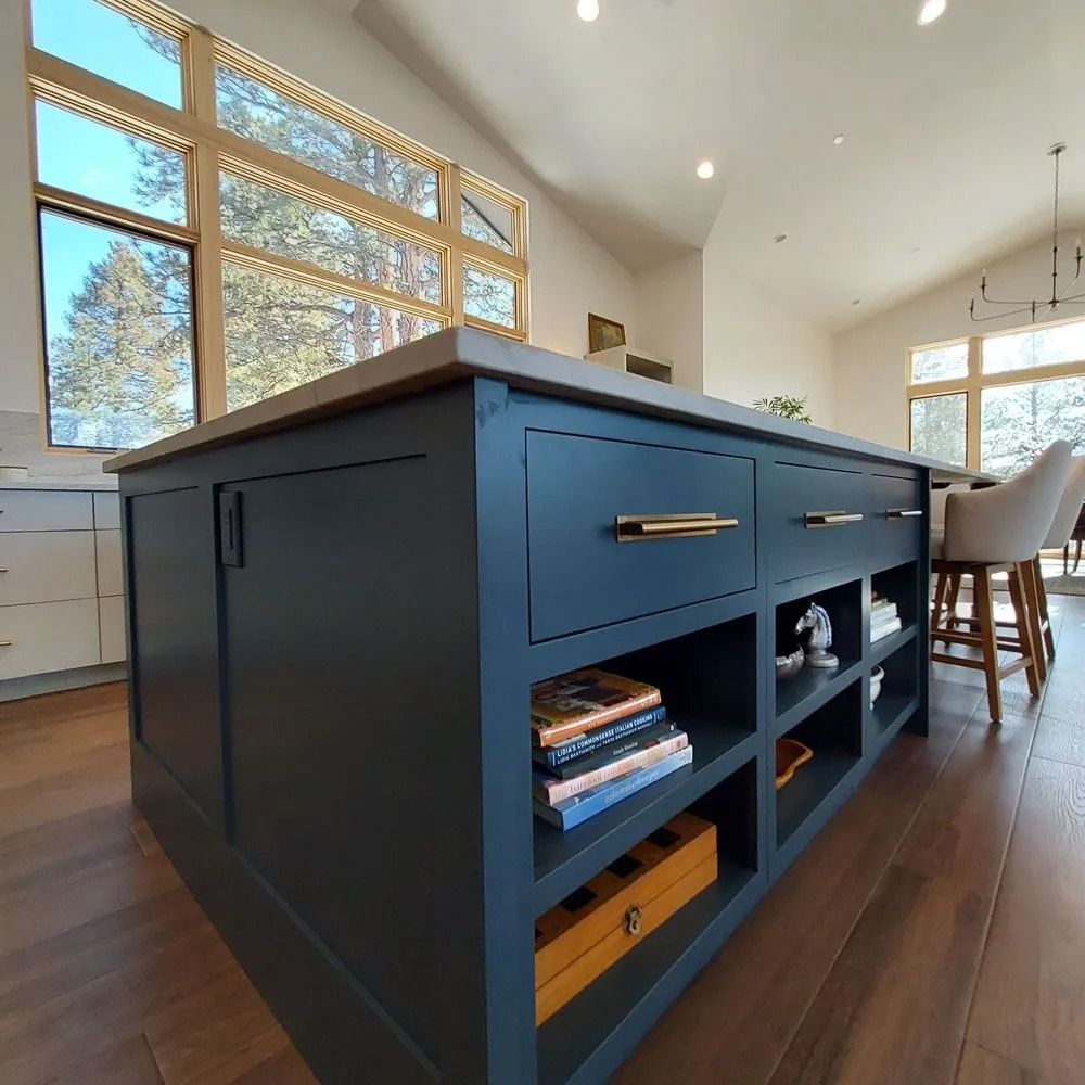 Blue kitchen island with open shelving, drawers, and concrete countertop.  Books and décor displayed.  Wood flooring.