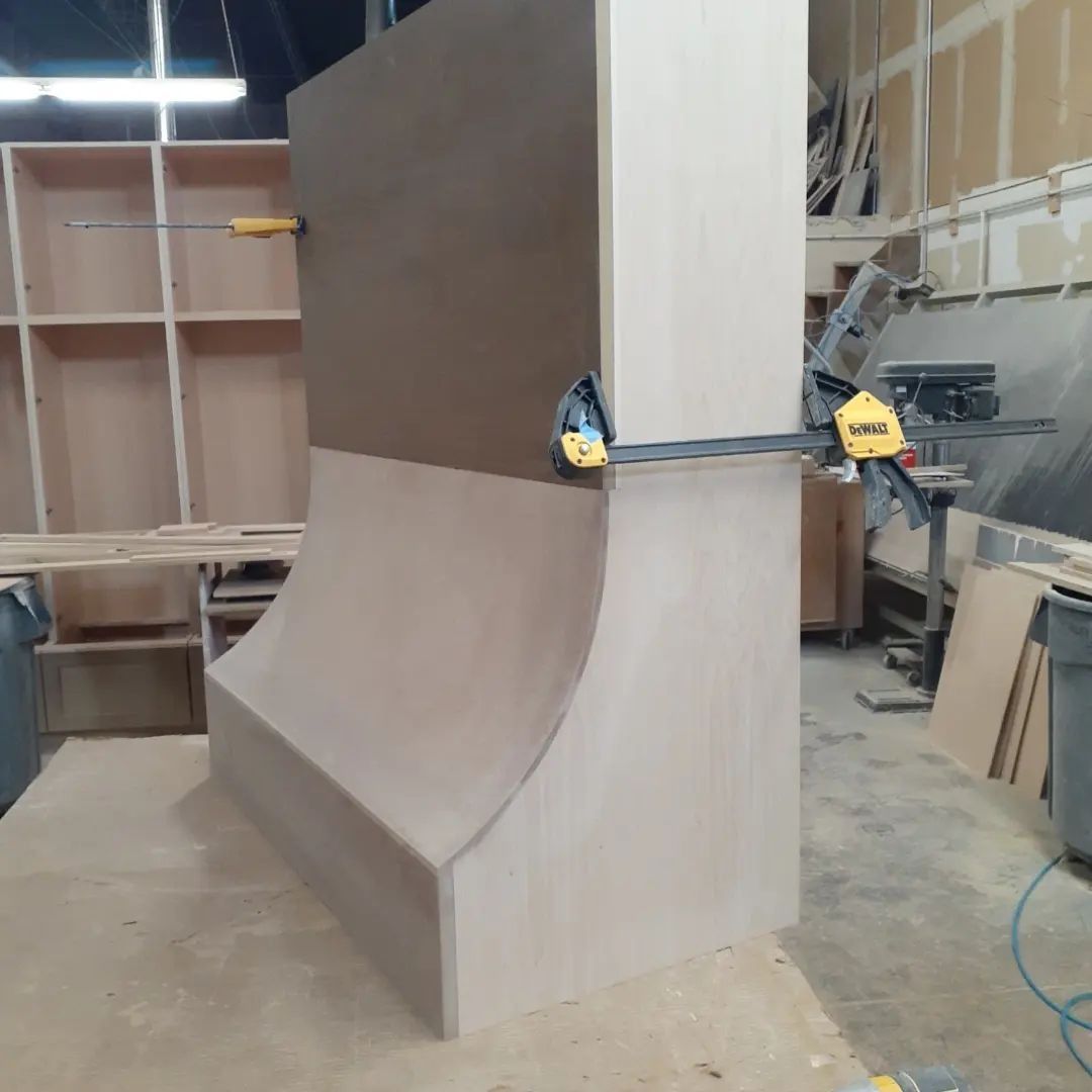 Large wooden structure under construction in a workshop, clamped together with yellow clamps.