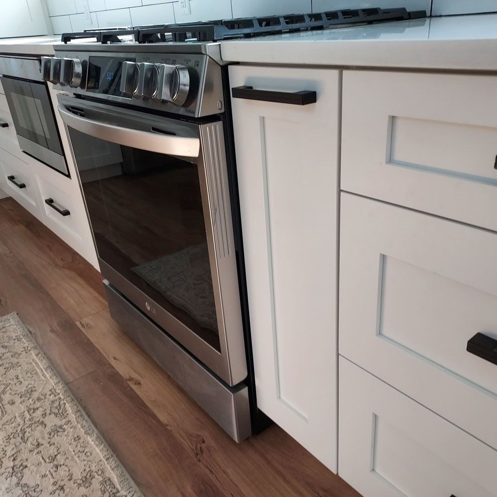 Stainless steel stove and white cabinets in a kitchen, with black handles and a light countertop.