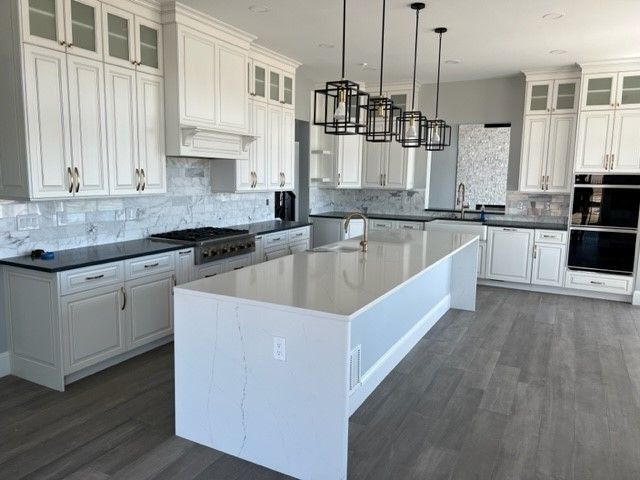White kitchen with island, cabinets, dark countertops, and pendant lights.