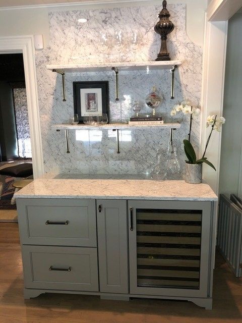 Gray bar cabinet with marble countertop and matching backsplash, shelving, wine cooler, and decorative items.