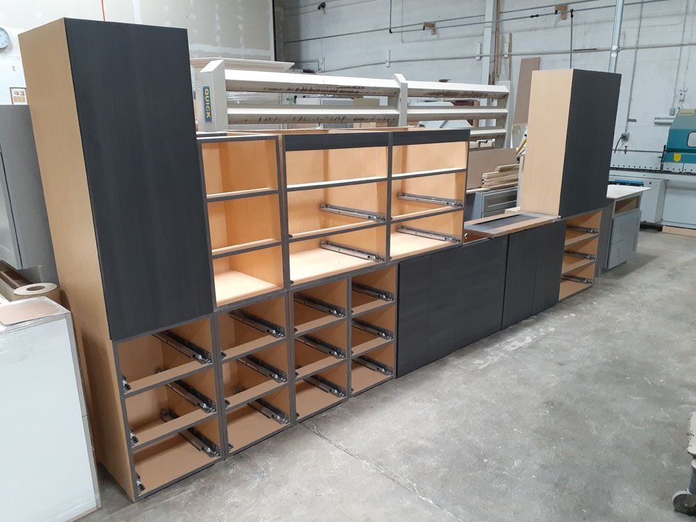Assembled unfinished cabinets in a workshop. Some have dark gray panels, others are beige.