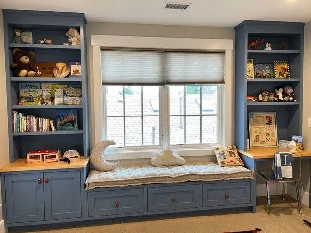 Blue built-in bookshelves frame a window seat with storage, holding toys and books.