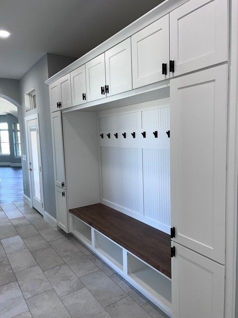 White built-in entryway storage with bench, hooks, and cabinets. Black hardware against white trim, wood bench.