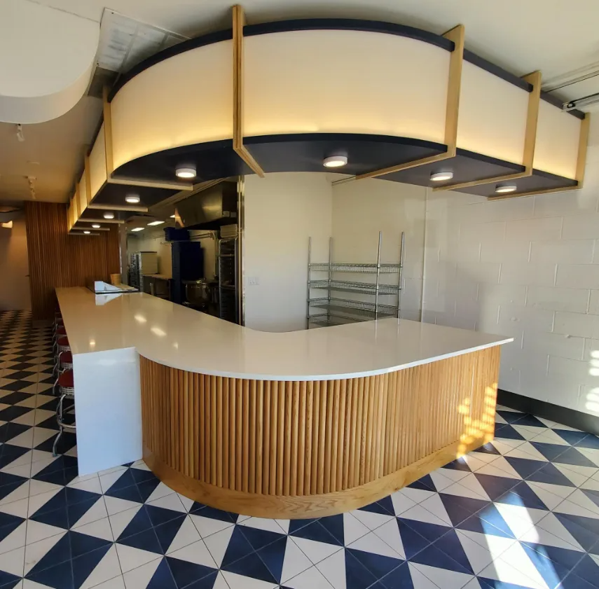 Restaurant interior with curved wood counter, checkered floor, and kitchen in background.