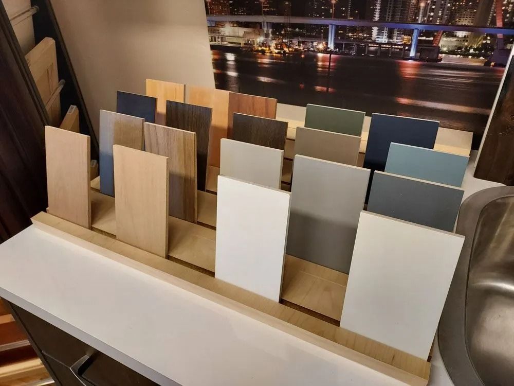 Display of wood and painted samples in various colors, arranged on a rack. Cityscape in background.