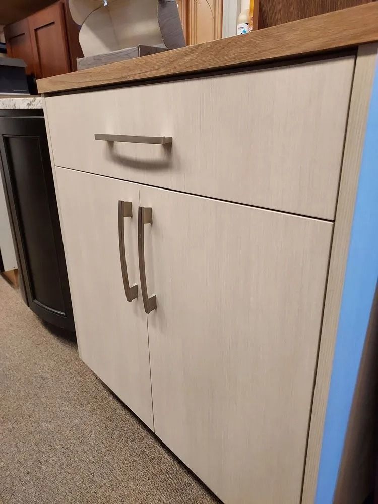 Light wood cabinet with a drawer and two doors, silver hardware, and a wood countertop.