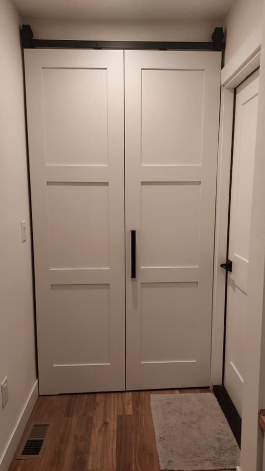 White double barn doors on a black track, with a black handle, in a hallway.