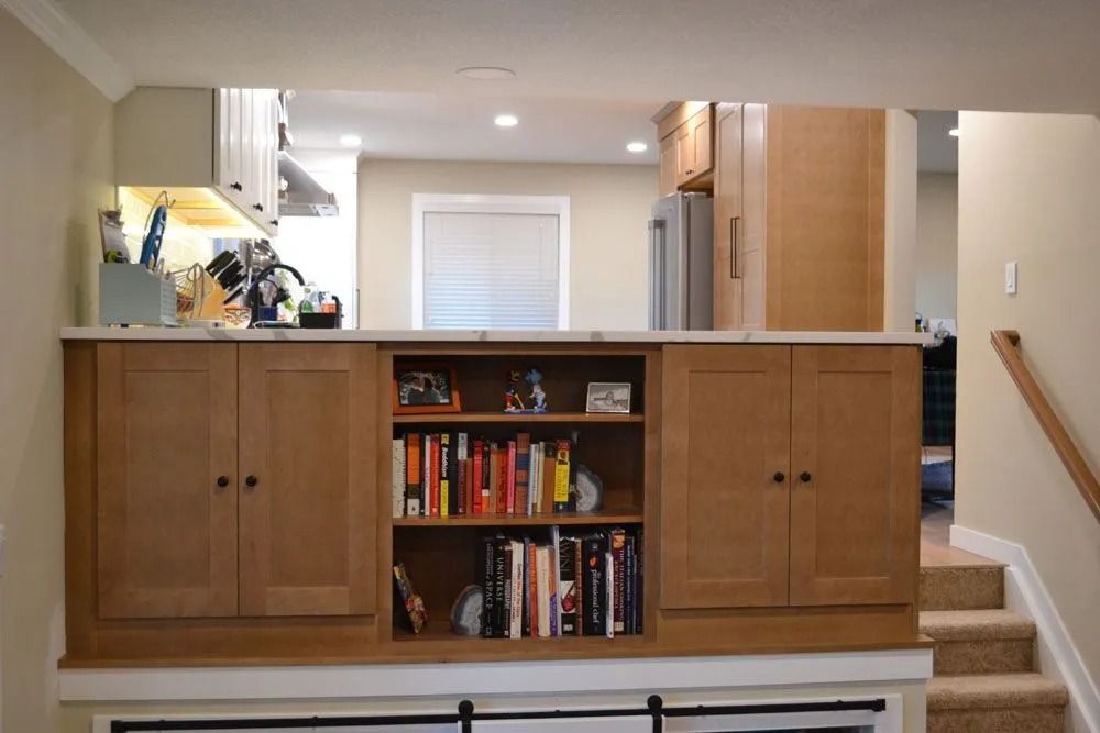 Built-in wooden bookcase with cabinets, counter, and opening to a kitchen and stairs.