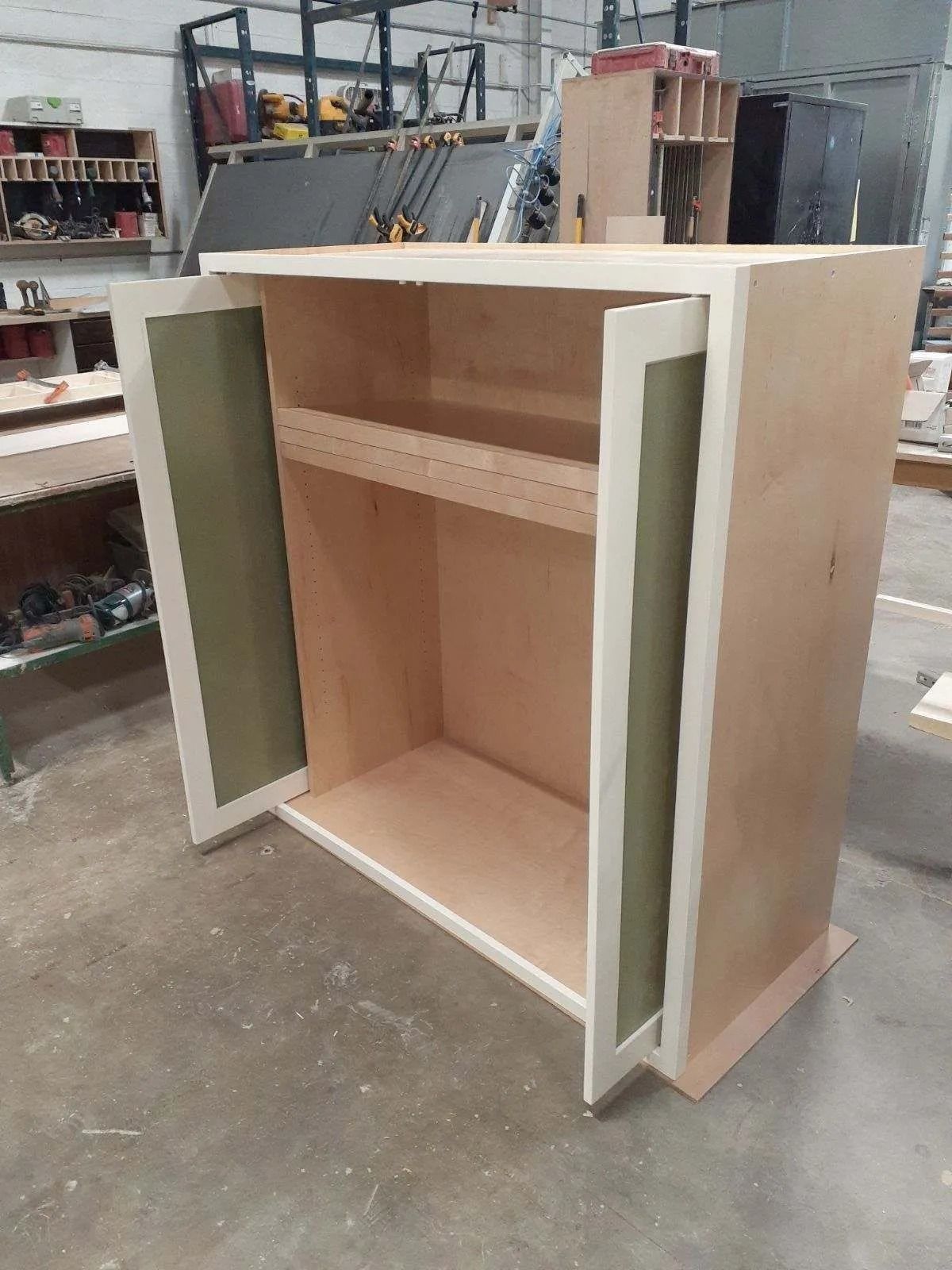 Cabinet with open doors, beige wood with white trim, interior shelf, workshop setting.