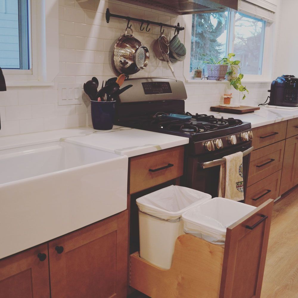 Kitchen with a white farmhouse sink, gas range, and pull-out trash bins. Brown cabinets and light countertops.