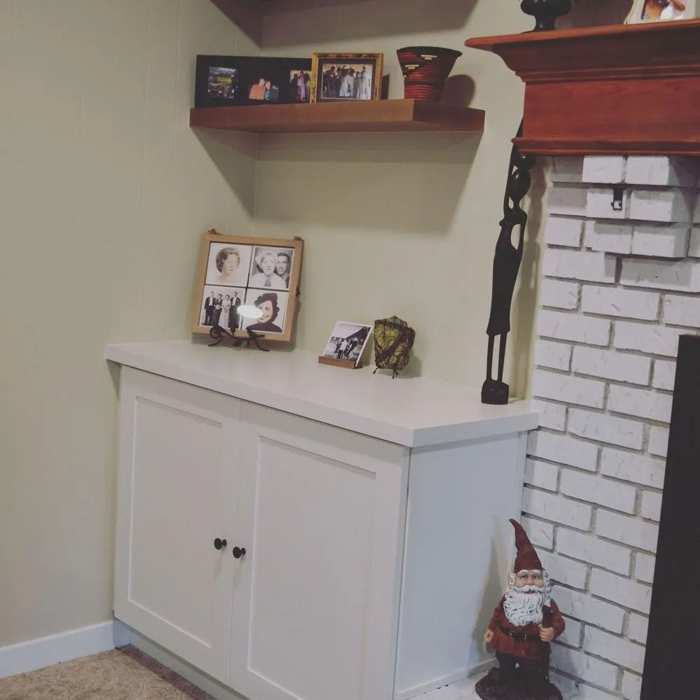 White cabinet with black knobs and decor on top and shelves on a light green wall.