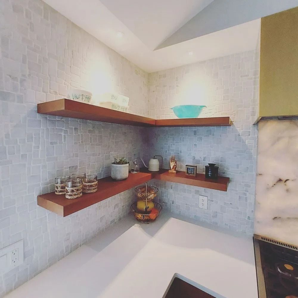 Wooden shelves in a kitchen corner, displaying dishes, plants, and other items against a mosaic tile backdrop.