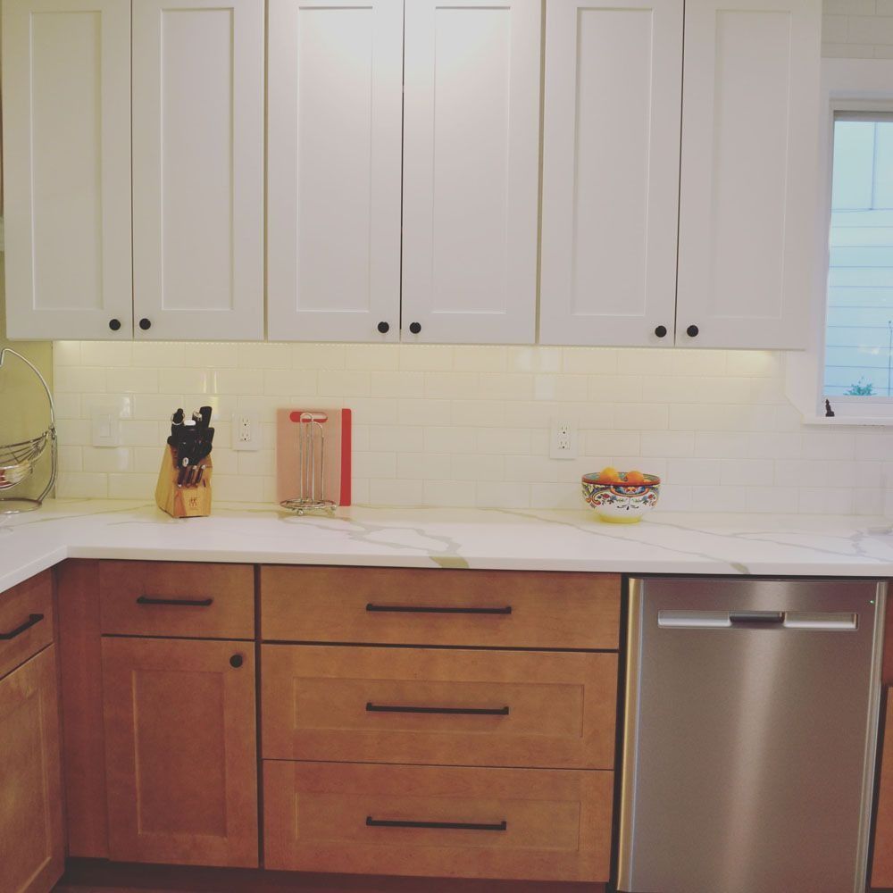 Kitchen with white upper cabinets, light wood lowers, white countertops, and stainless steel dishwasher.