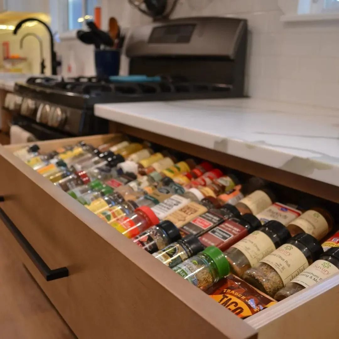 Open kitchen drawer filled with various spice jars, arranged for easy access.
