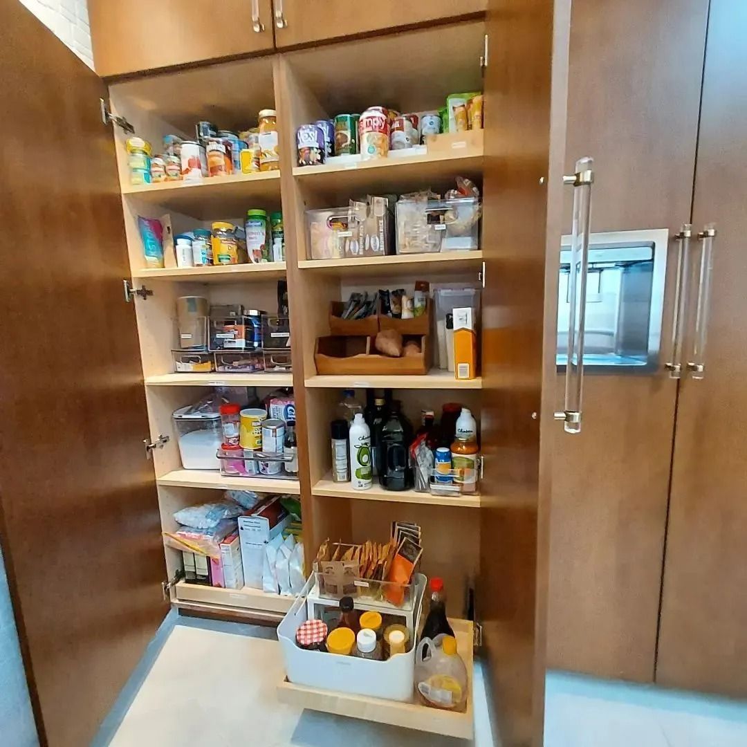Wooden pantry with open doors, shelves stocked with various food items and supplies. Pull-out shelf at the bottom.