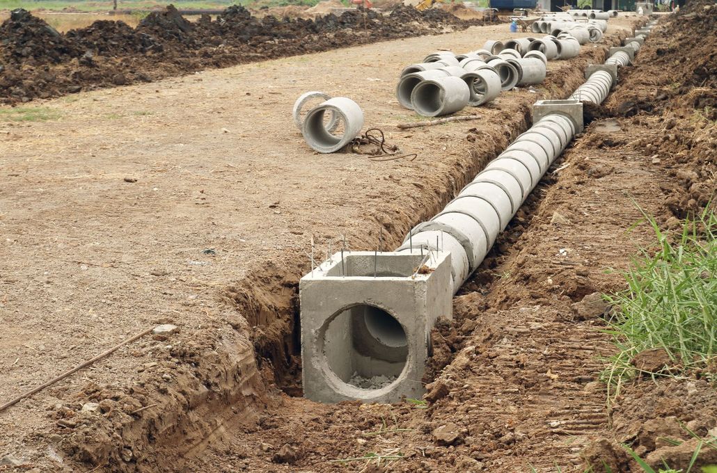 Concrete drainage pipes laid in a trench at a construction site, with one pipe section in the foreground.