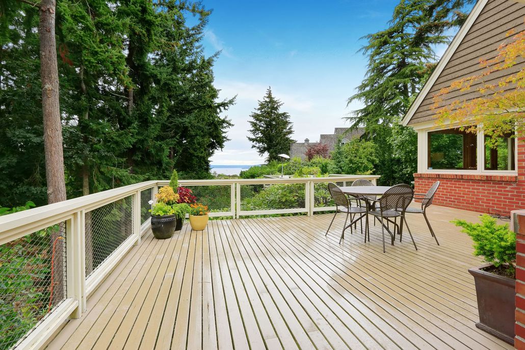Wooden deck with patio table, potted plants, and treetop ocean view beside a brick house