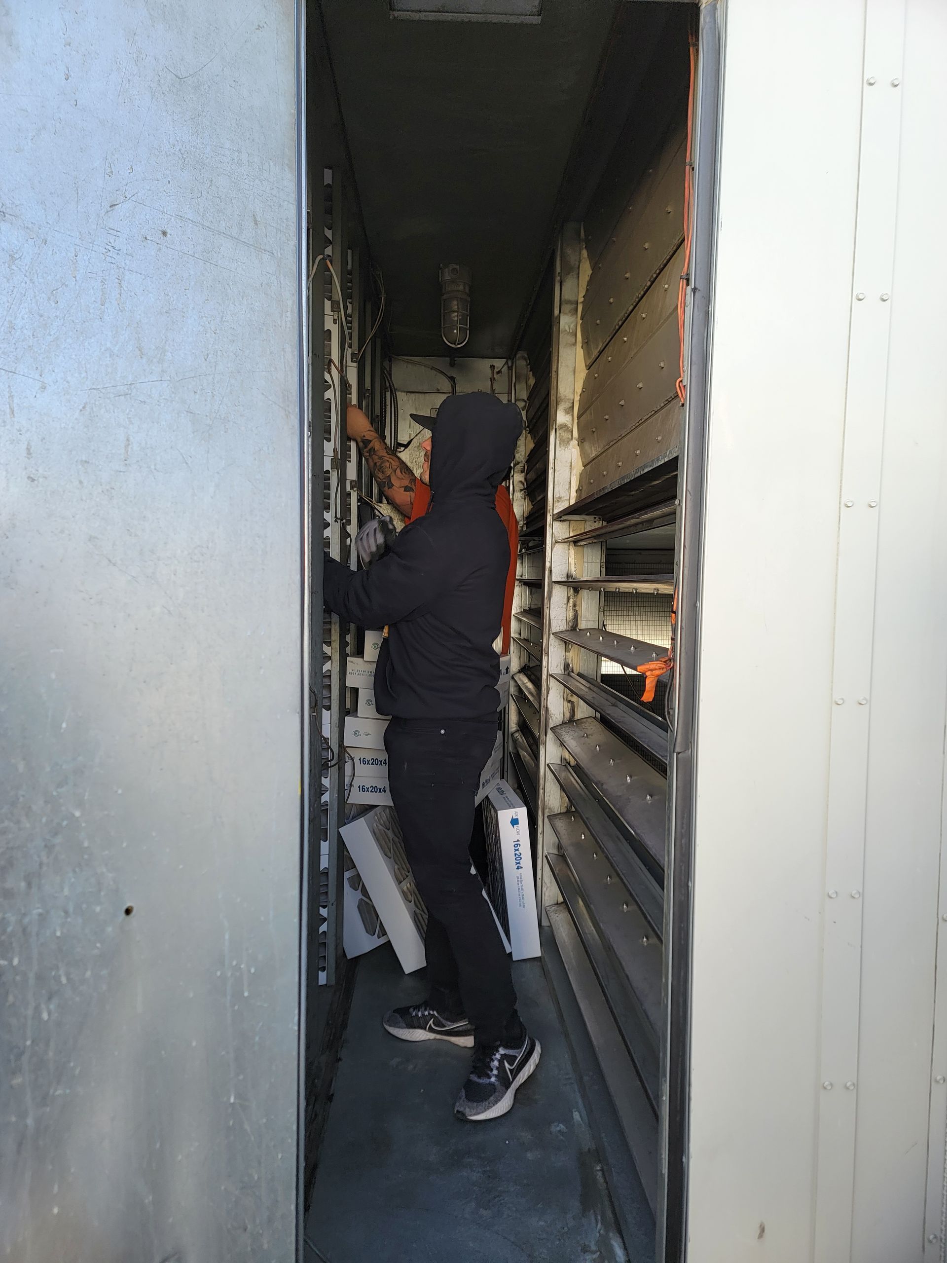 A hand holding a dirty air filter from a white air vent. Filter is full of black particles.