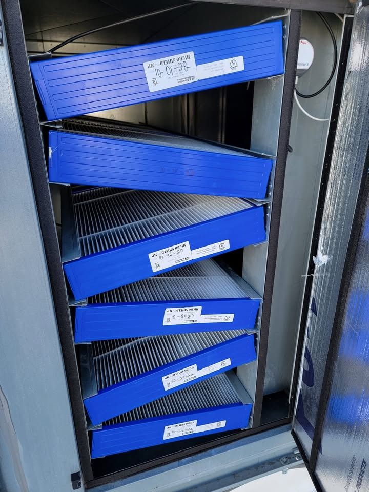 Blue air filters stacked inside a metal ventilation unit.
