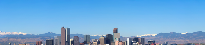 City skyline under a blue sky with snow-capped mountains in the background.