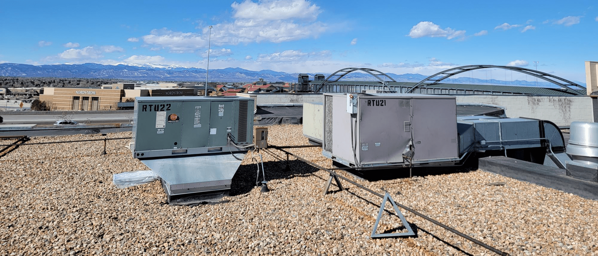 Rooftop with air conditioning units, urban view with mountains and bridge under a blue sky.