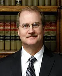 Man in suit and tie in front of a bookshelf, posing in an office