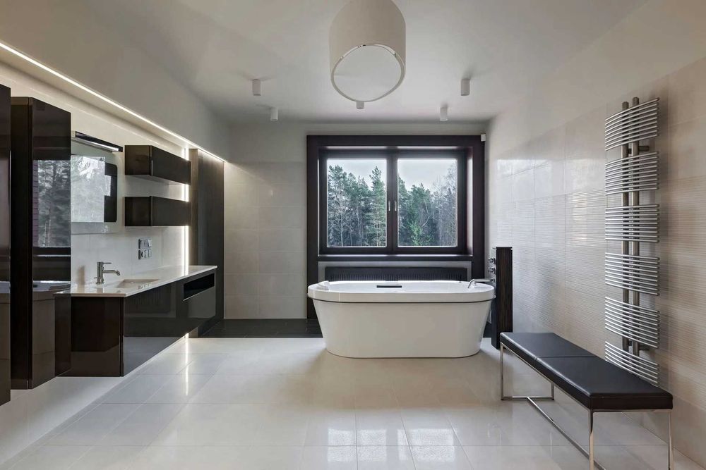 Modern bathroom with white tub, dark cabinetry, window, and large tiled wall.