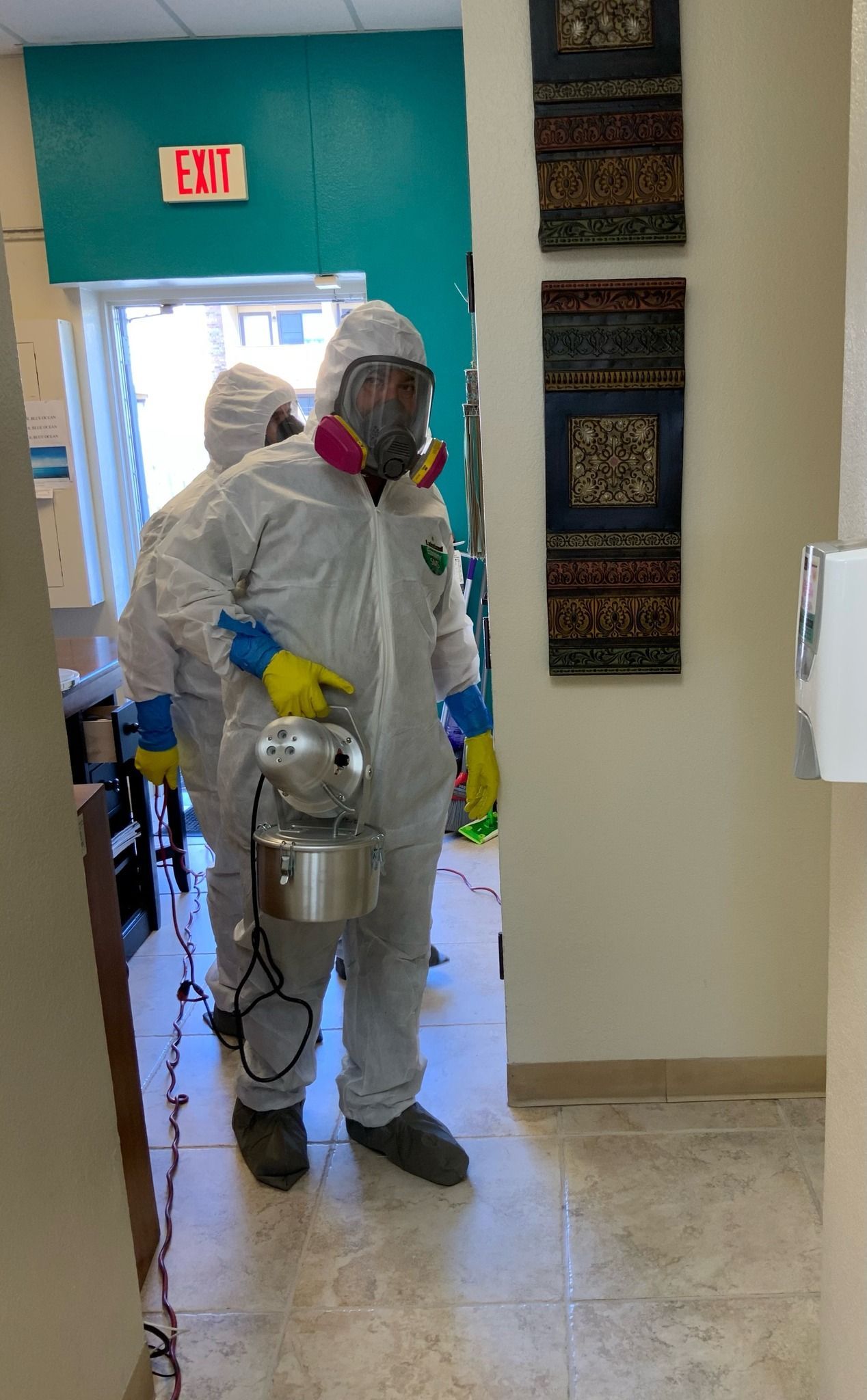 A man in a protective suit is spraying a room with a sprayer.