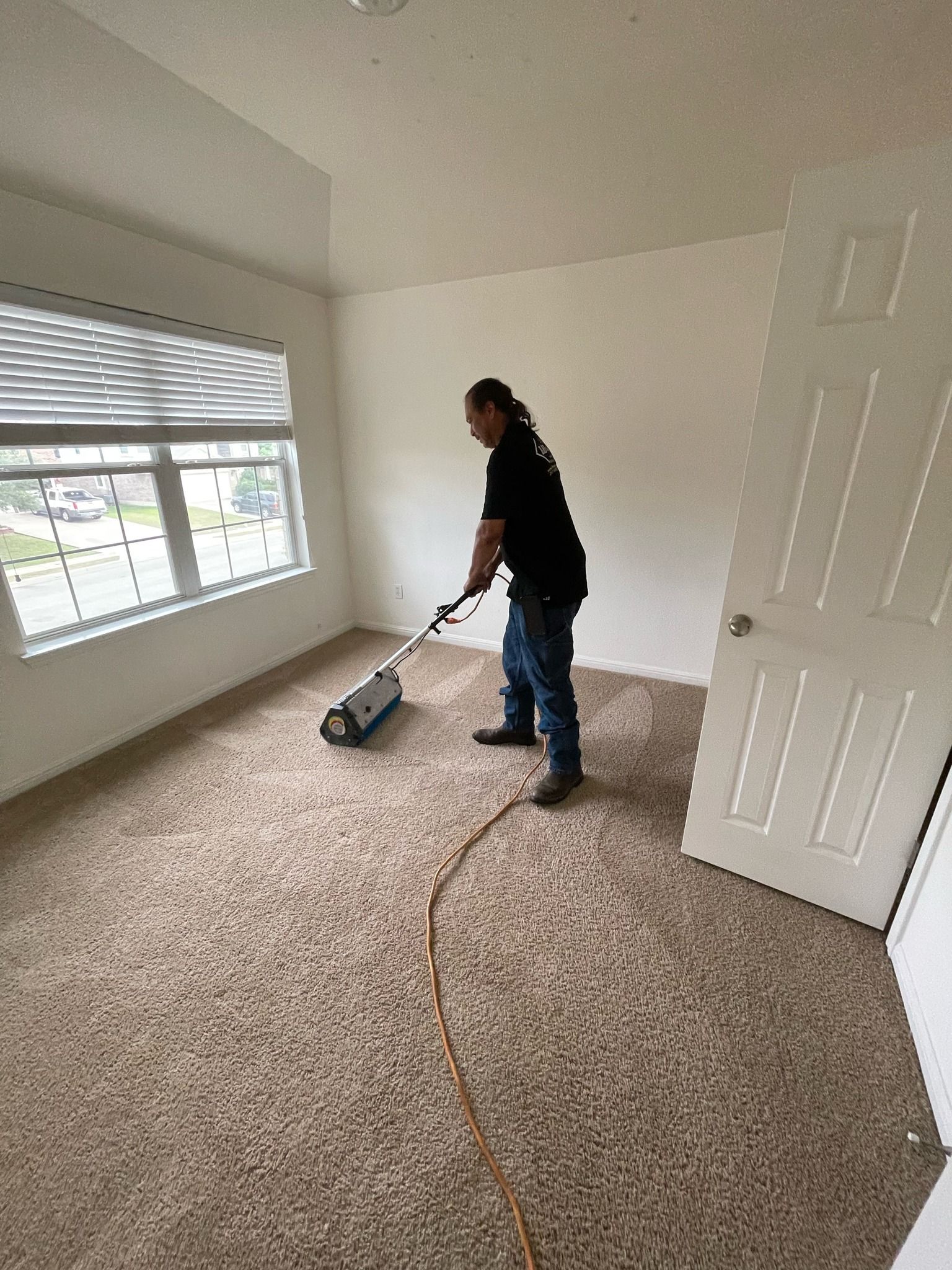 A man is cleaning a carpet in a bedroom with a vacuum cleaner.