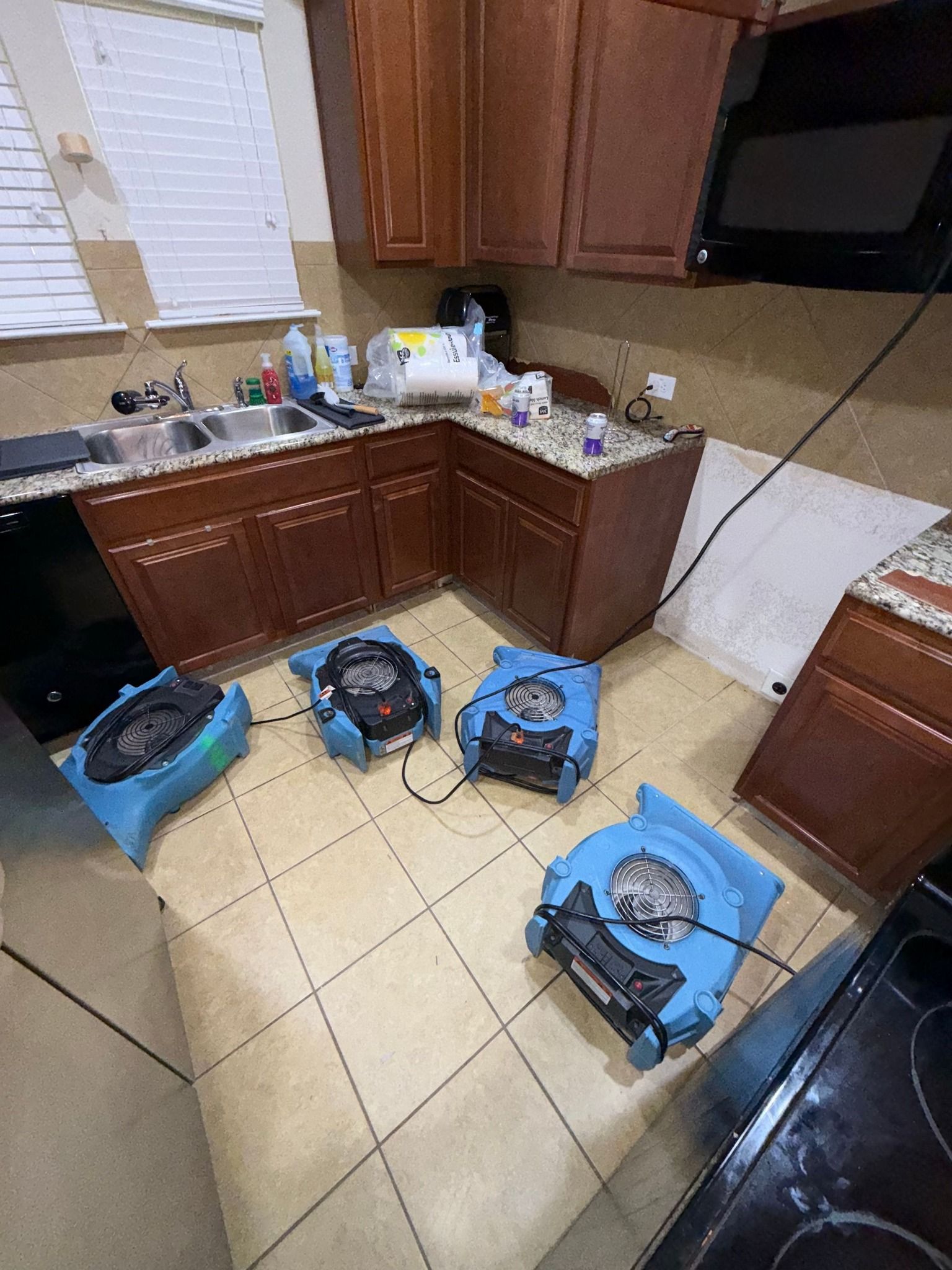 Three fans are sitting on the floor of a kitchen.