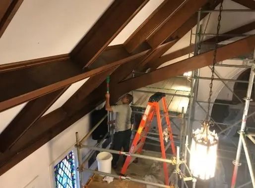 Workers on scaffolding inspecting a wooden beam ceiling in an unfinished attic interior