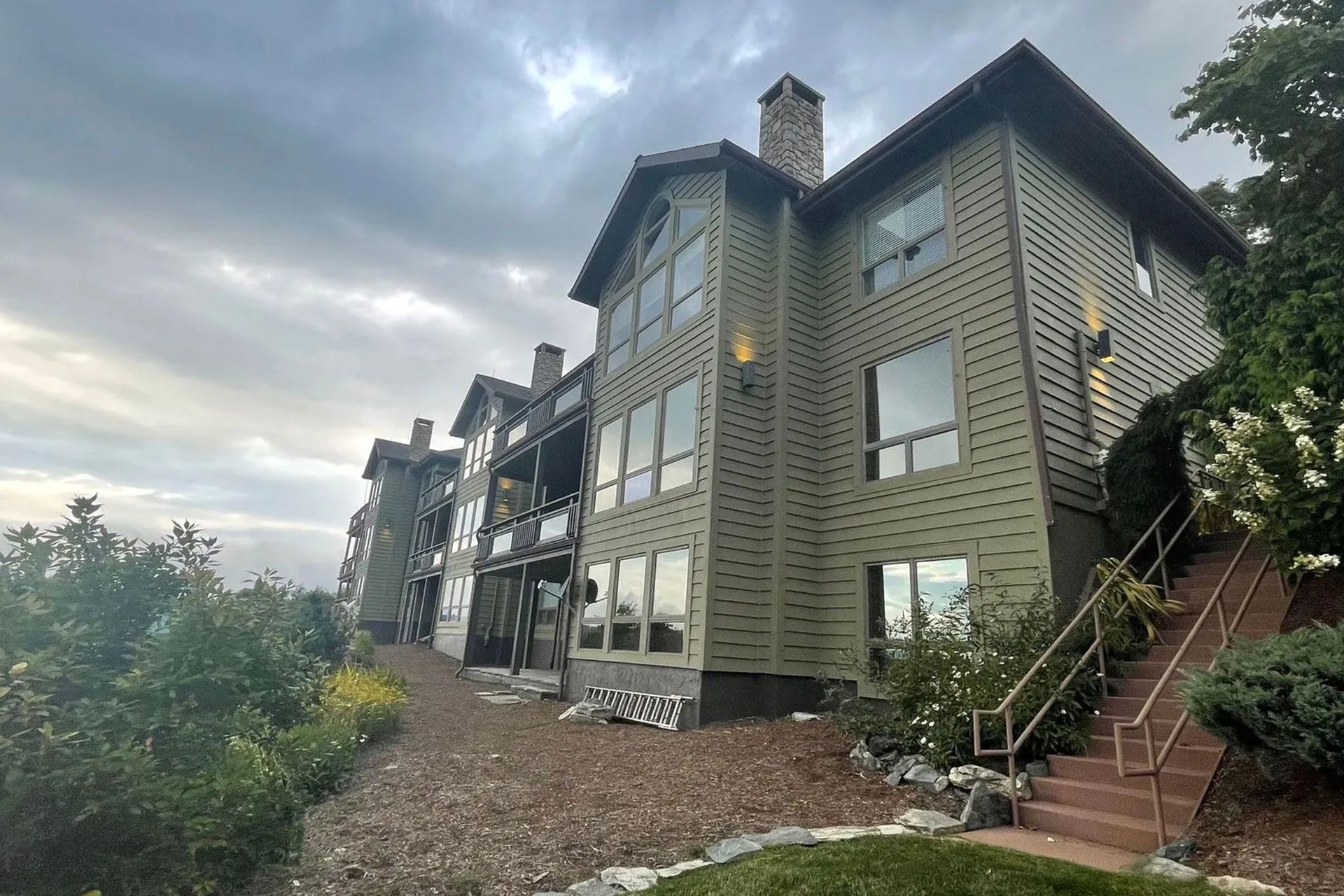 Multi-story lodge-style building with stone and wood exterior, viewed from a landscaped hillside with stairs.