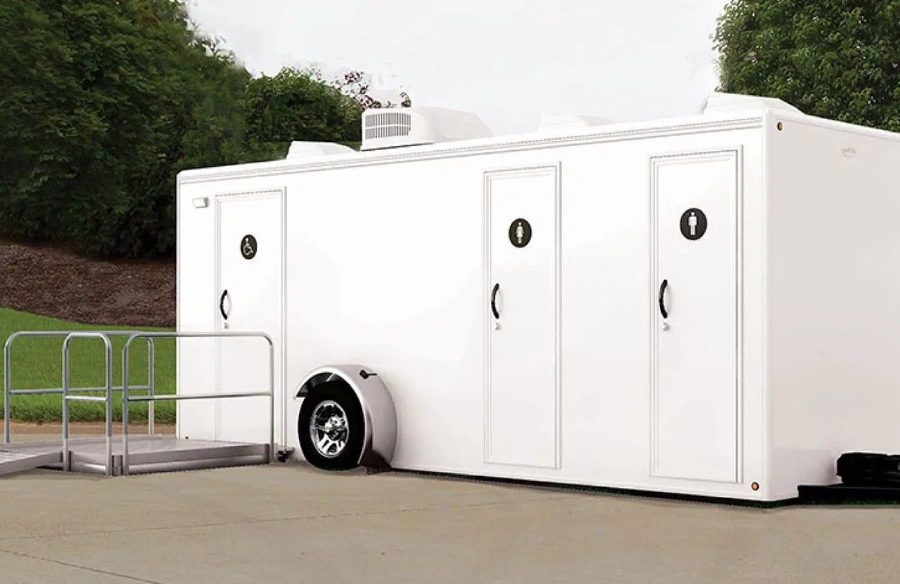 White portable restroom trailer with four doors and a ramp.