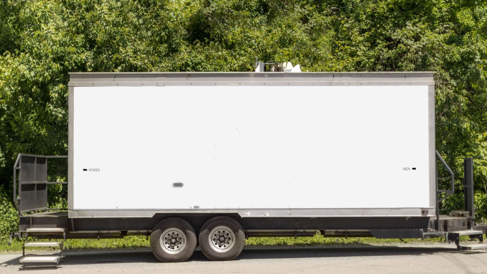 A white portable bathroom trailer is parked on the side of the road