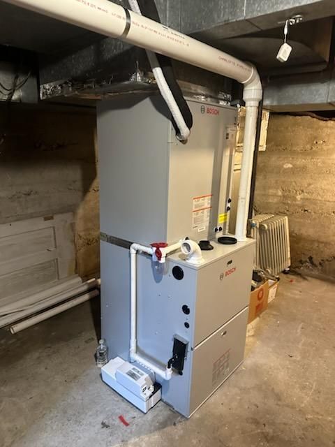 A white furnace is sitting in a basement next to pipes.