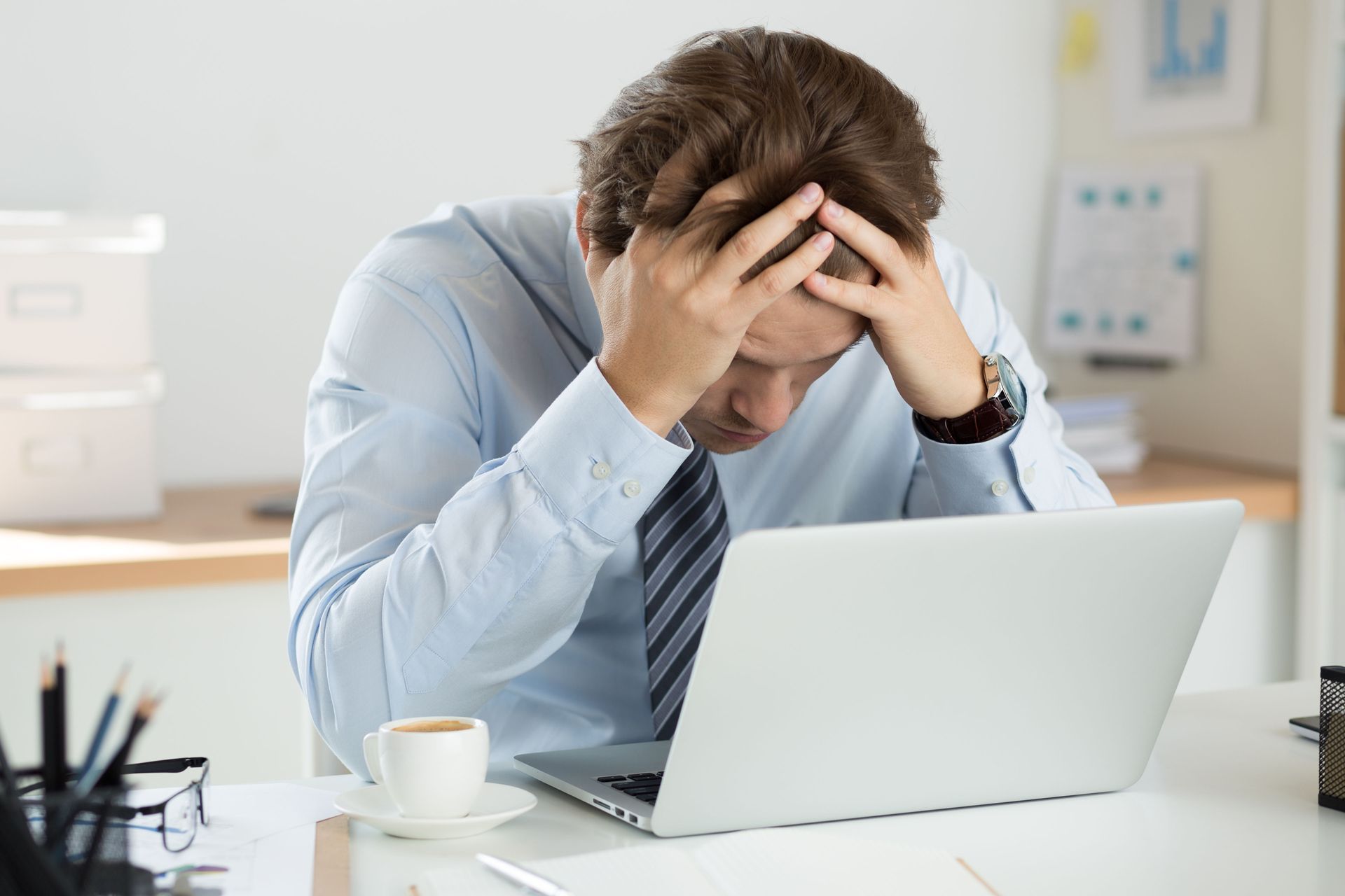 Man in office shirt with hands on head looking at laptop; stressed.